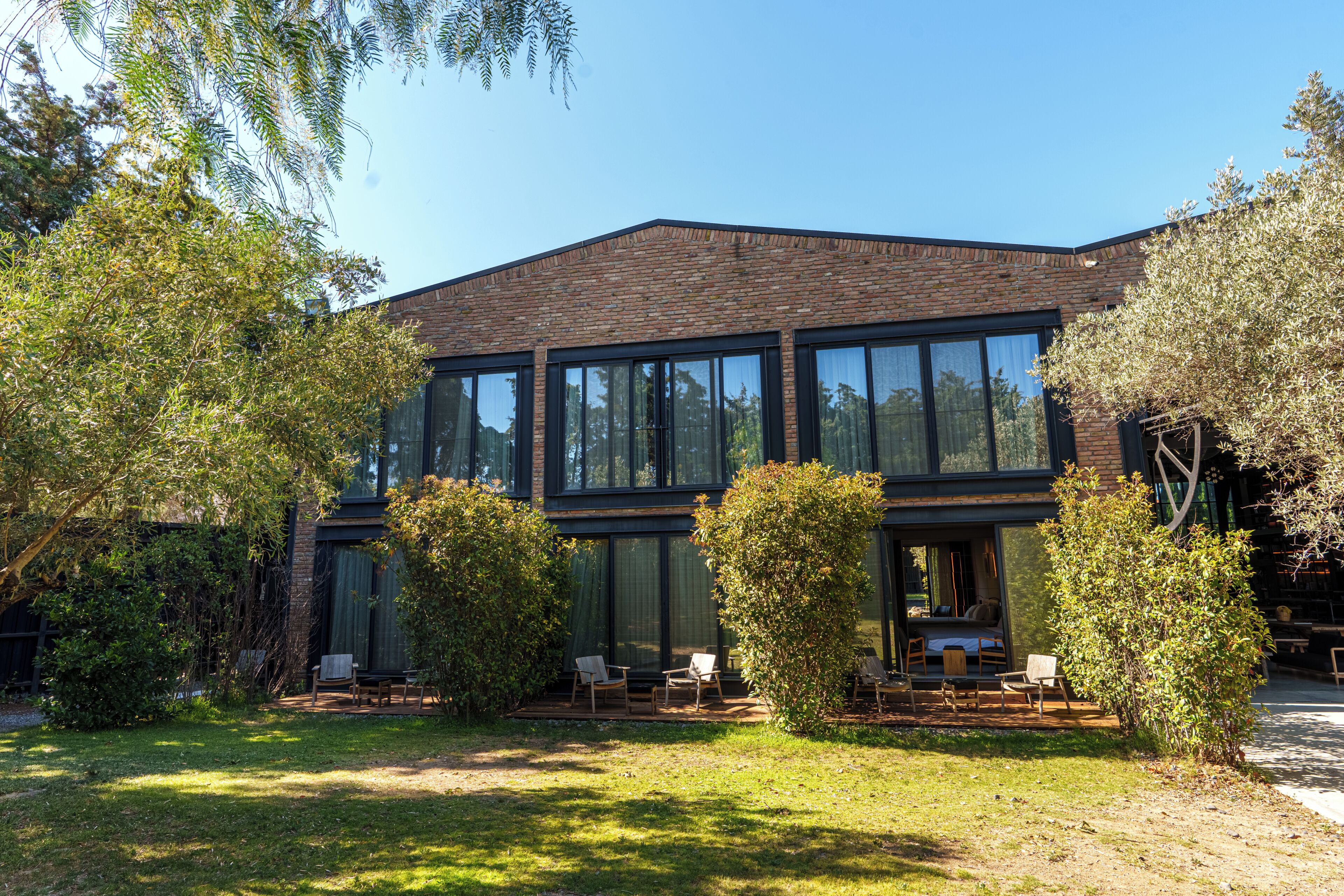 Ein modernes Gebäude mit großen Fenstern, einer Ziegel-Fassade und einem gepflegten Garten mit Außenplätzen.