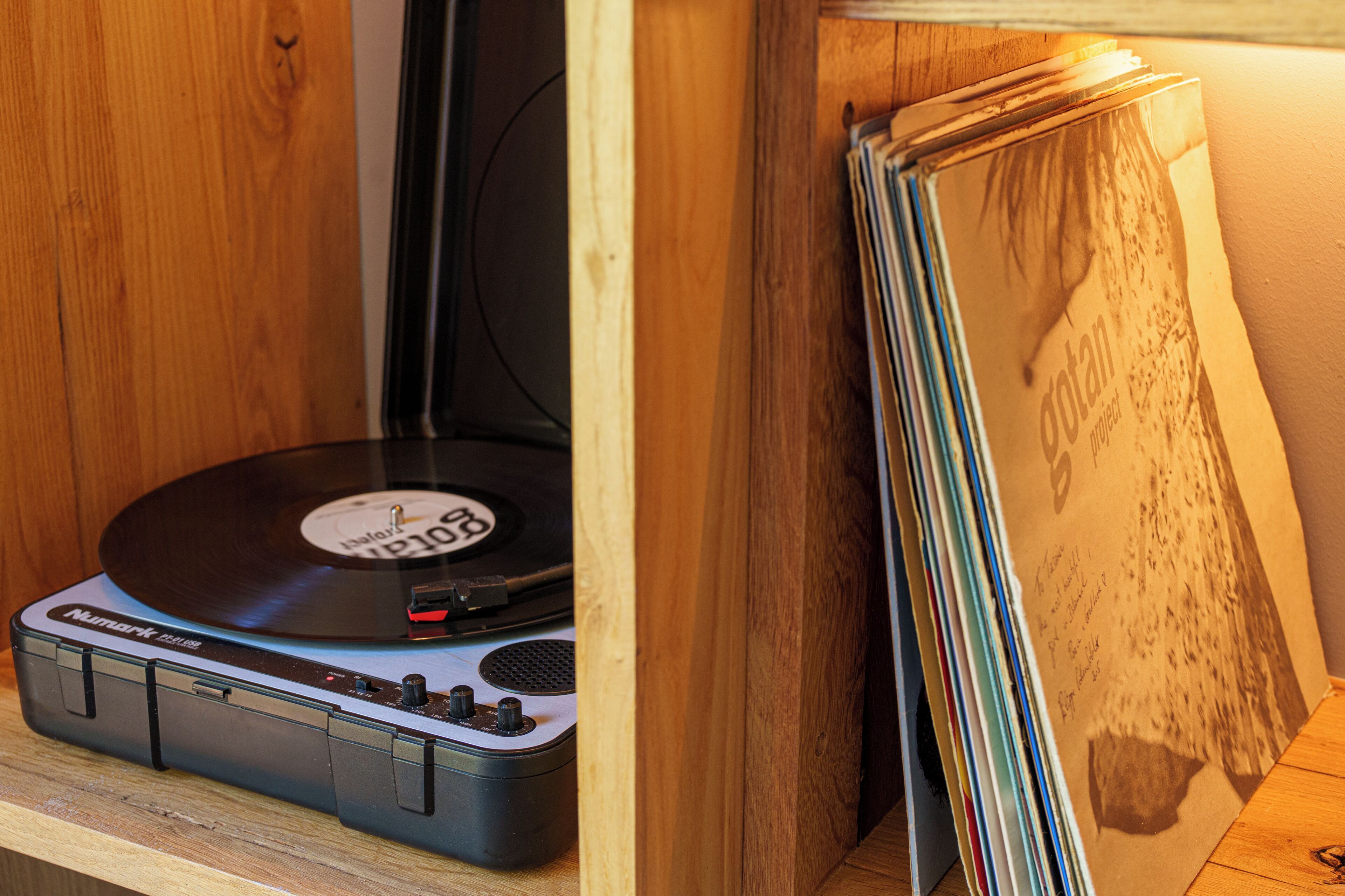 Tocadiscos con un disco de vinilo, una pila de revistas y un mueble de madera.