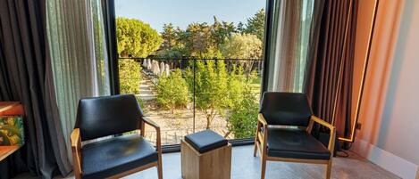 A room with two black chairs, a small wooden table, and a view of a garden through large windows.