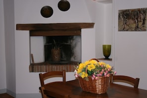 A dining area with a wooden table, chairs, a fireplace, and a basket of flowers.
