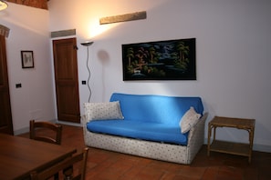 A living room with a blue sofa, a small table, a wooden door, and a painting on the wall.