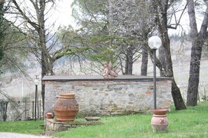 A rustic stone structure with a statue on top, surrounded by trees and a lamp post.