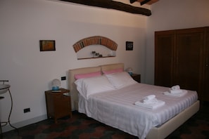 A bedroom with a bed, a nightstand, a small shelf, and a wooden wardrobe.