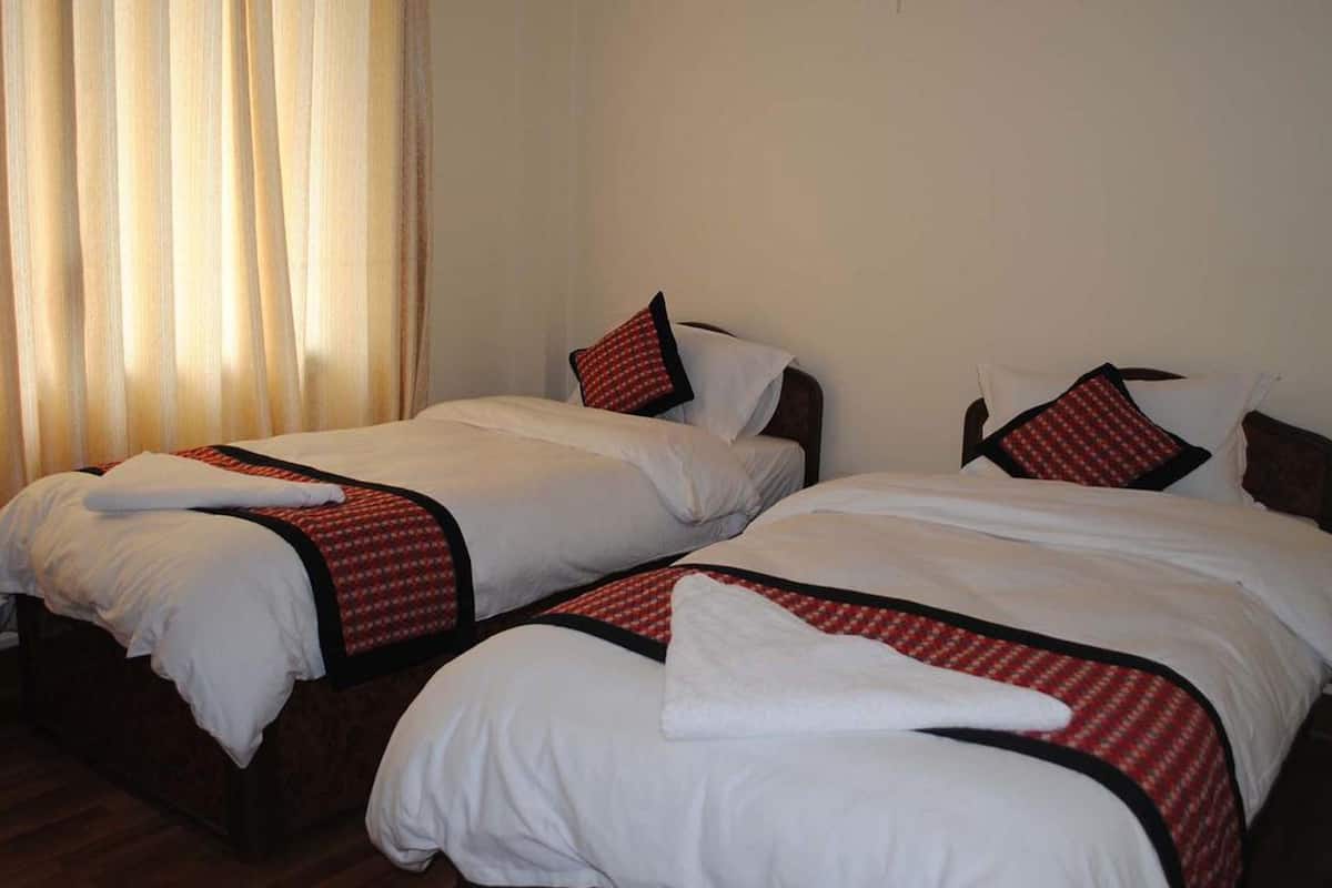 A hotel room with two single beds, each with white linens and red and black patterned bedspreads.