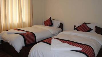 A hotel room with two single beds, each with white linens and red and black patterned bedspreads.