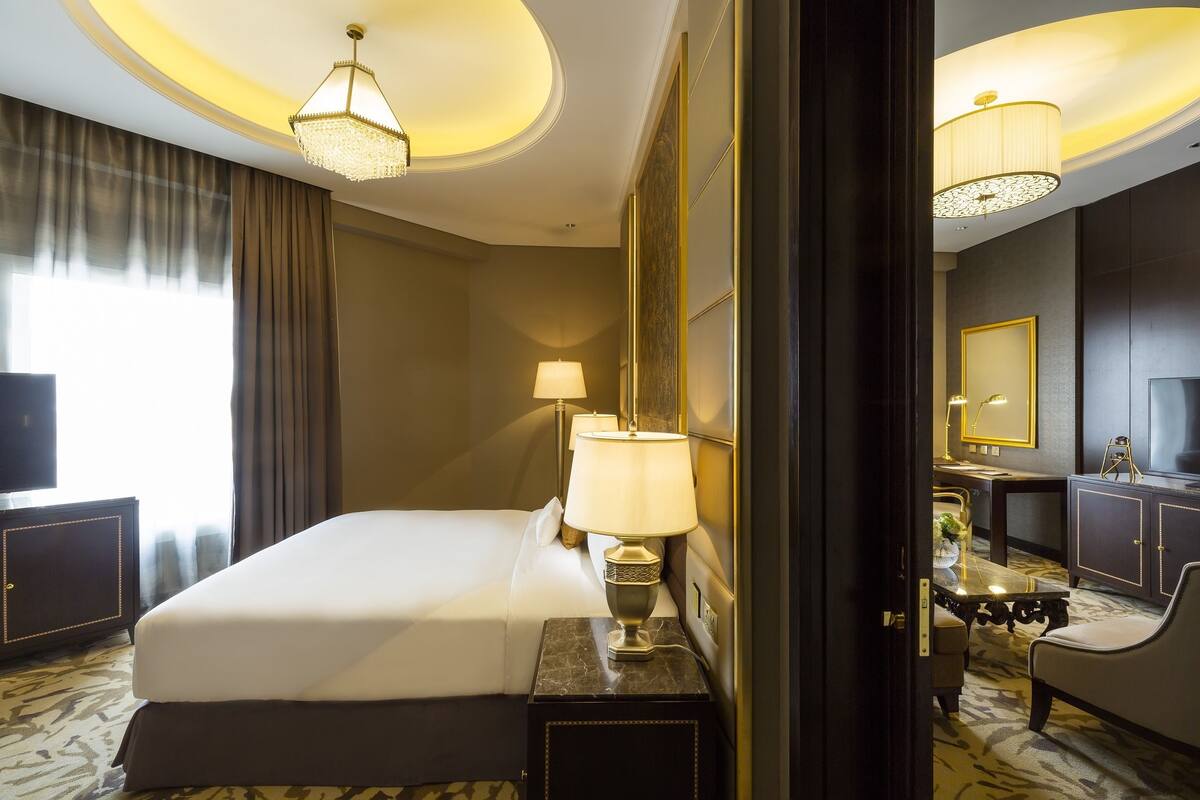 A hotel room with a large bed, a bedside table with a lamp, a desk with a chair, and a television.