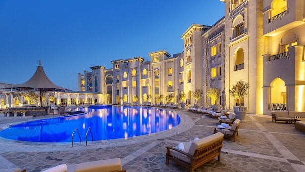 A pool area with lounge chairs and a building with arched windows and balconies. - Ezdan Palace Hotel (Doha)