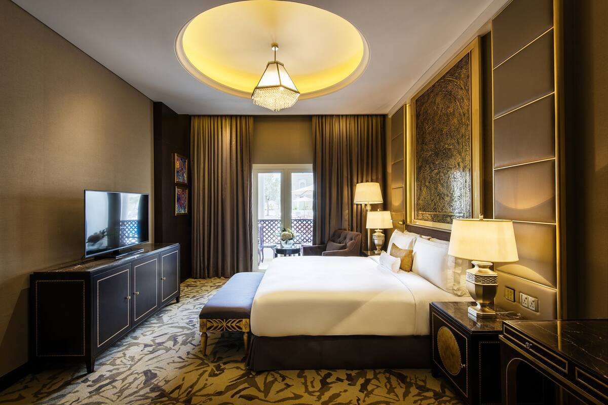 A hotel room with a large bed, a television on a cabinet, a desk with a lamp, and a view of the outdoors through a window.