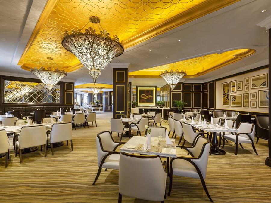 Un comedor amplio con varias mesas y sillas, candelabros ornamentales y obras de arte enmarcadas en las paredes.