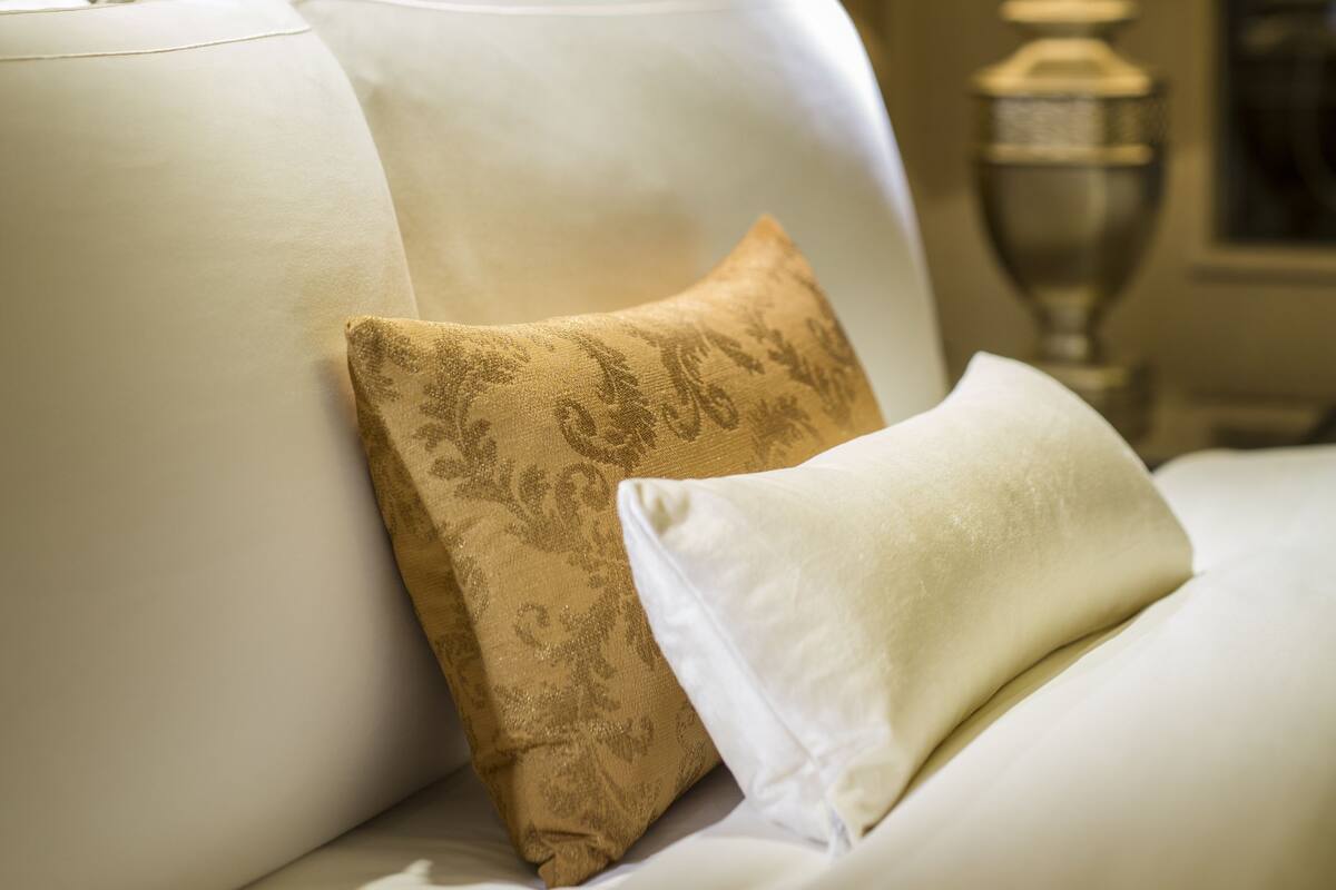A neatly made bed with white and patterned pillows, a lamp, and a framed artwork on the wall.