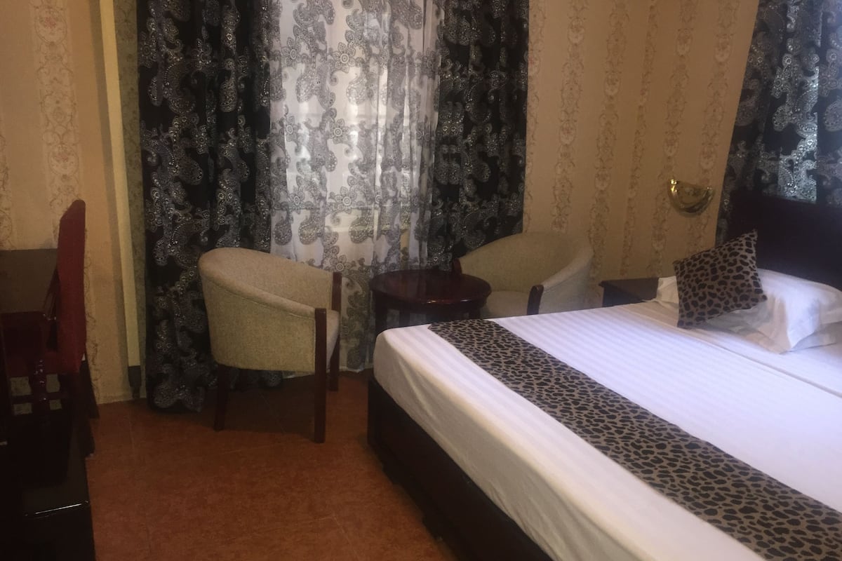 A hotel room with a bed, two chairs, a small table, and patterned curtains.