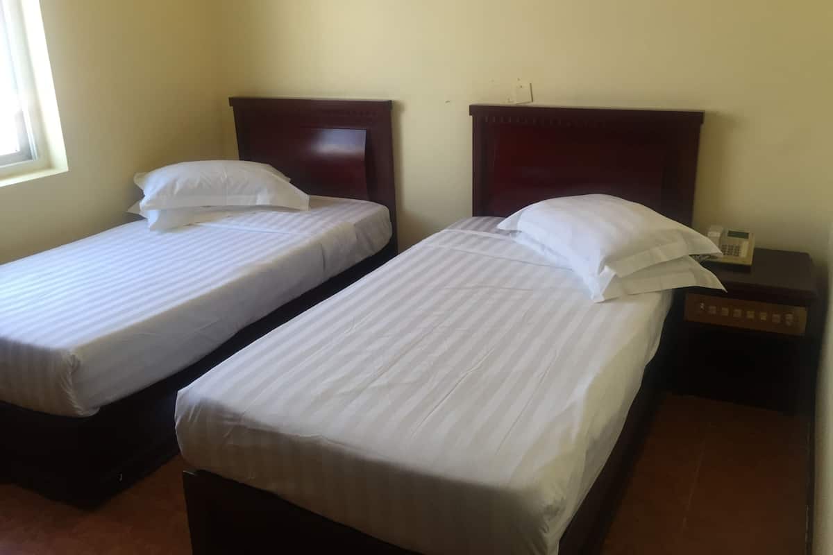Two single beds with wooden headboards in a room with plain walls and a tiled floor.
