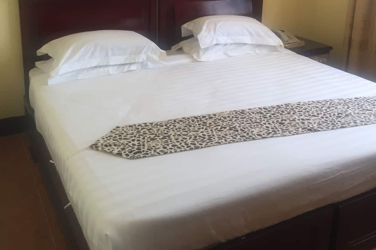 A bed with white linens, a dark wooden headboard, and a leopard print throw. There are two framed pictures on the wall above the bed.