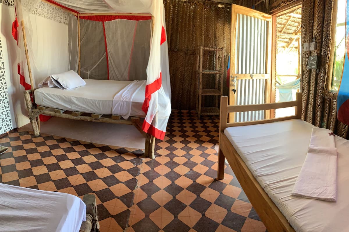 Um quarto com piso xadrez, uma cama com mosquiteiro e uma cadeira de madeira.