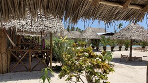 A beachside area with thatched umbrellas, wooden seating, and tropical plants. - New Jambo Bungalows - Hostel (Paje)