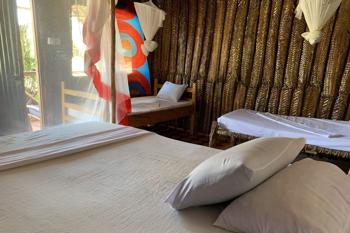 Quarto com duas camas, uma com dossel e outra sem. Há uma cadeira de madeira e uma mesa pequena.