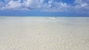 A boat on a clear, calm beach with a blue sky and scattered clouds. - New Jambo Bungalows - Hostel (Paje)