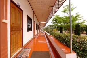 Un pasillo con una puerta de madera identificada con el número 101, piso de baldosas y una galería techada con barandilla de metal.