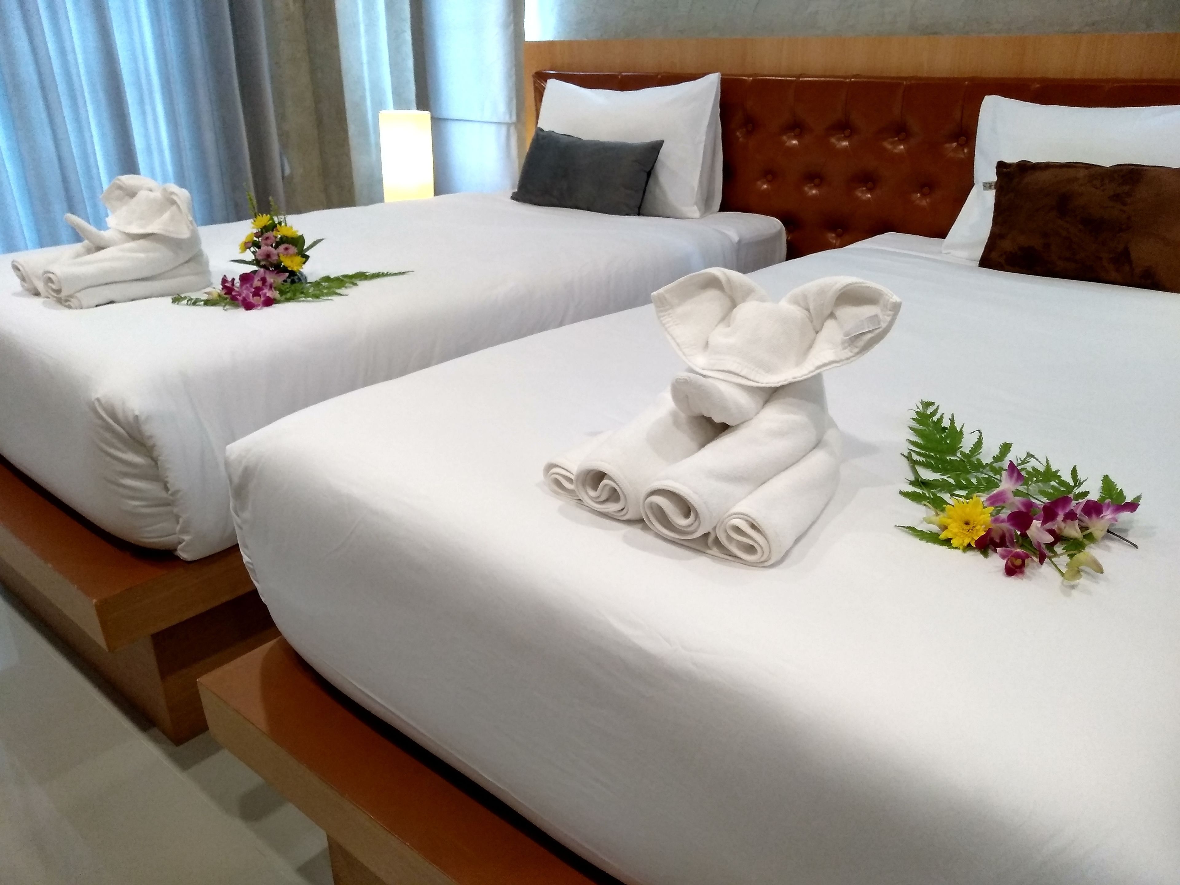 Two hotel beds with neatly folded towels and floral arrangements.