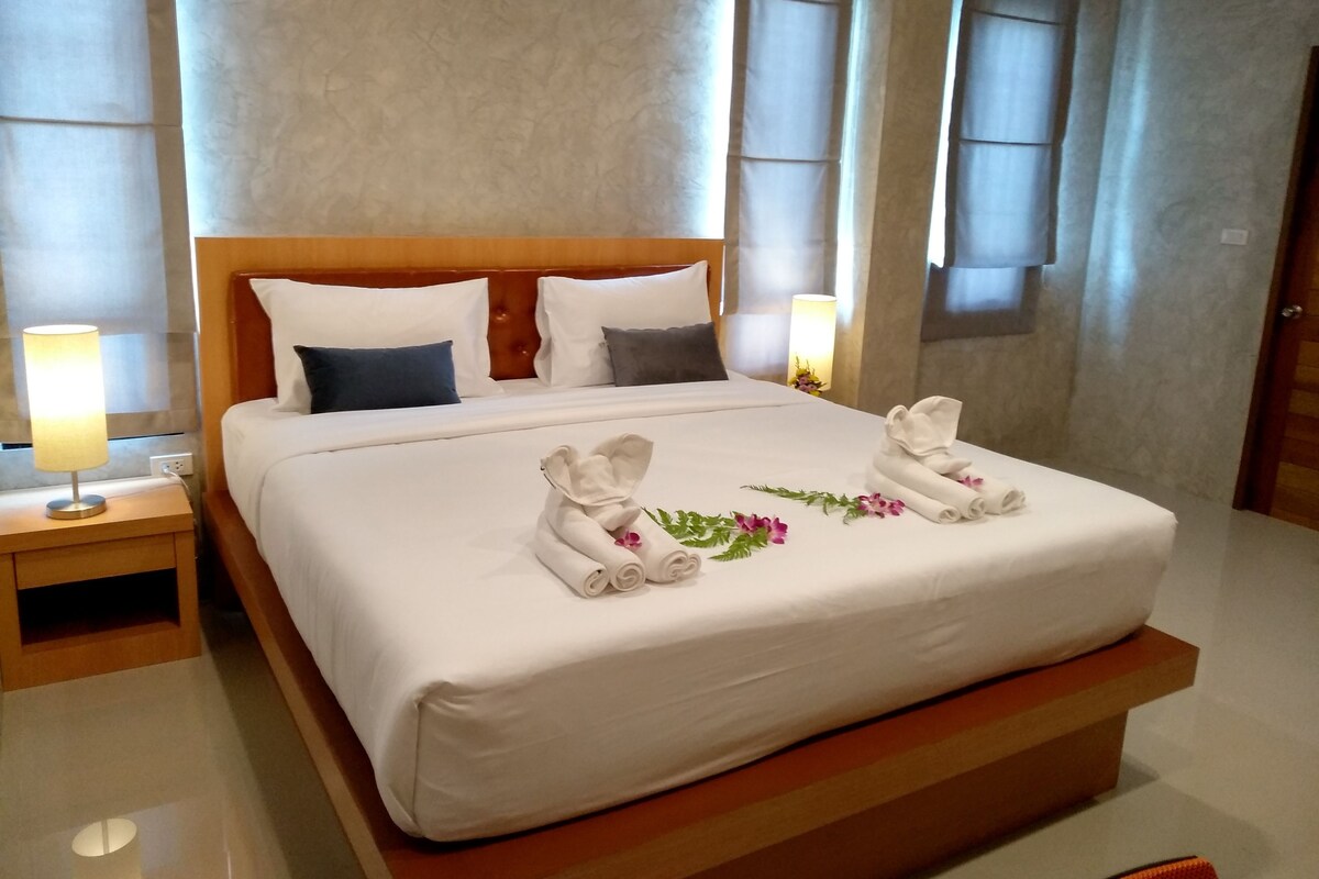 A neatly made bed with white linens, pillows, and a decorative towel arrangement.