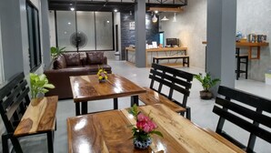 Un interior moderno con un área de comedor que incluye mesas de madera y sillas negras, un sofá y una recepción con una computadora.