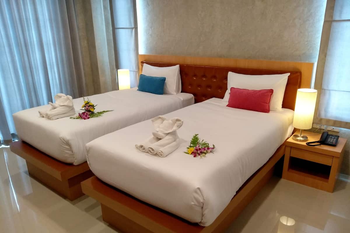 A hotel room with two beds, each with white linens, a wooden headboard, and a bedside table with a lamp and phone.