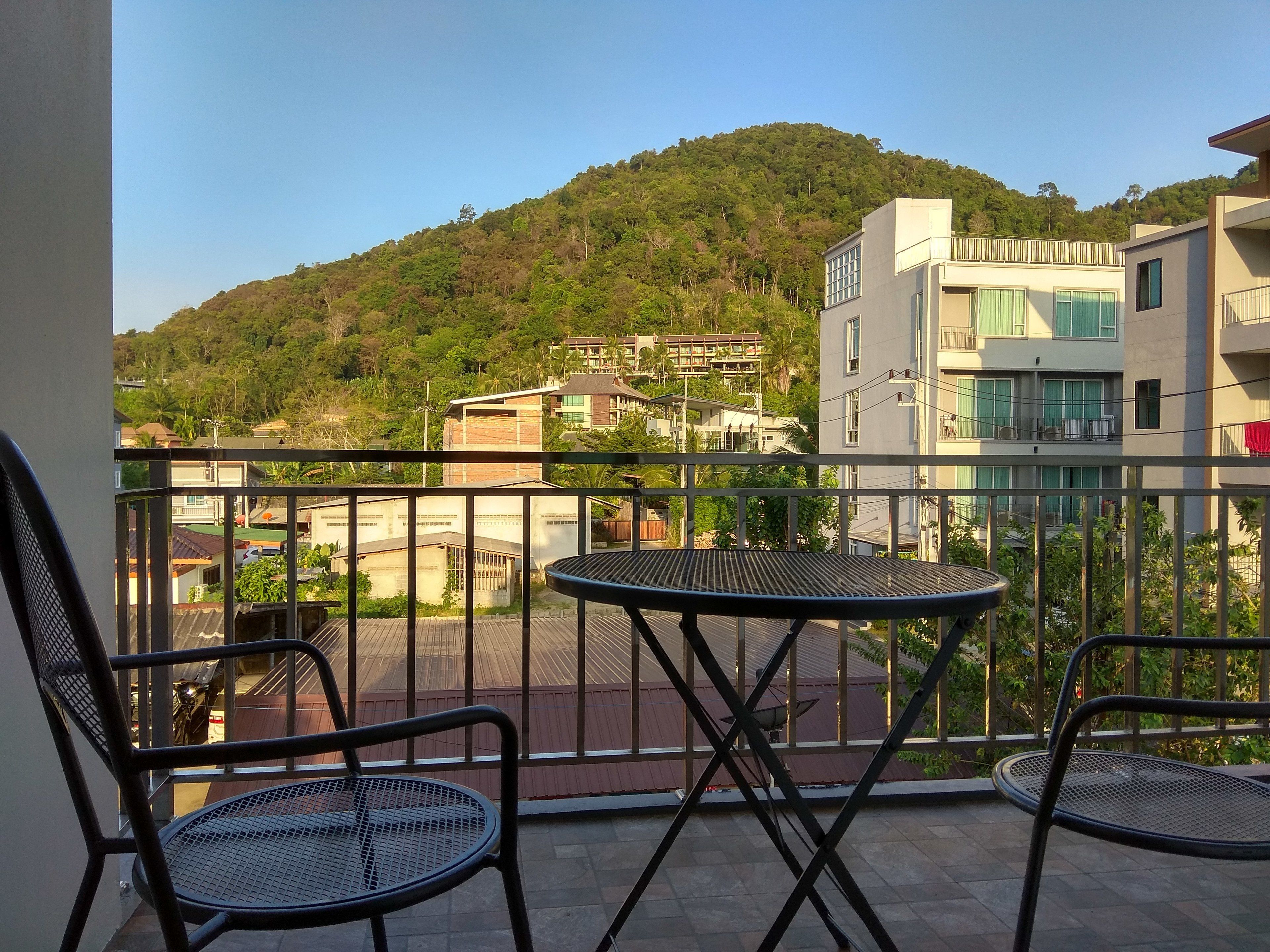 Un balcon avec deux chaises en métal et une petite table ronde, donnant sur une colline parsemée de bâtiments et de verdure.