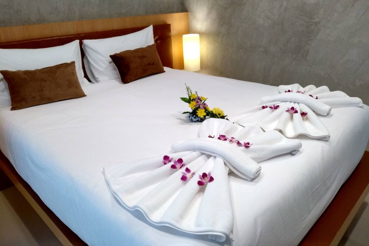 A neatly made bed with white linens, brown pillows, and a floral arrangement on the bed.