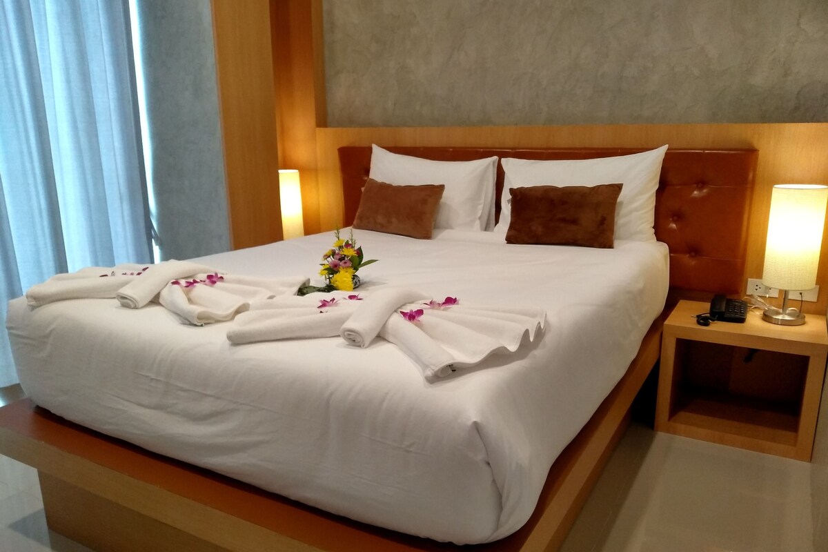 A hotel room with a large bed, white linens, a wooden headboard, two bedside lamps, and a small table with a phone and keys.
