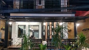 Un edificio moderno con vestíbulo cubierto, plantas en macetas y una zona de estar con bancos.