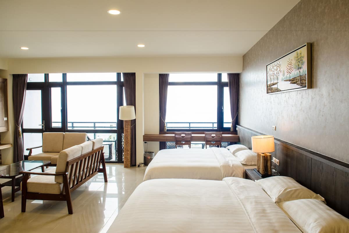 Une chambre d’hôtel avec deux lits, un canapé, un bureau et une grande fenêtre.
