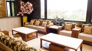 A living room with a sofa set, wooden coffee tables, and a large window with a view of greenery. - Hola sea view B&B (Shoufeng)