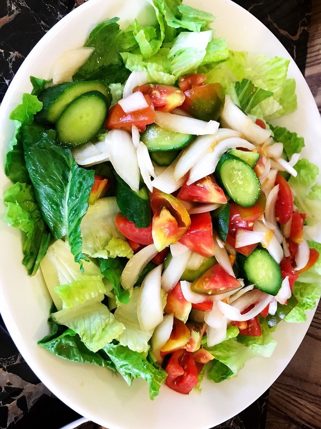 A bowl of salad with lettuce, cucumbers, tomatoes, and onions.