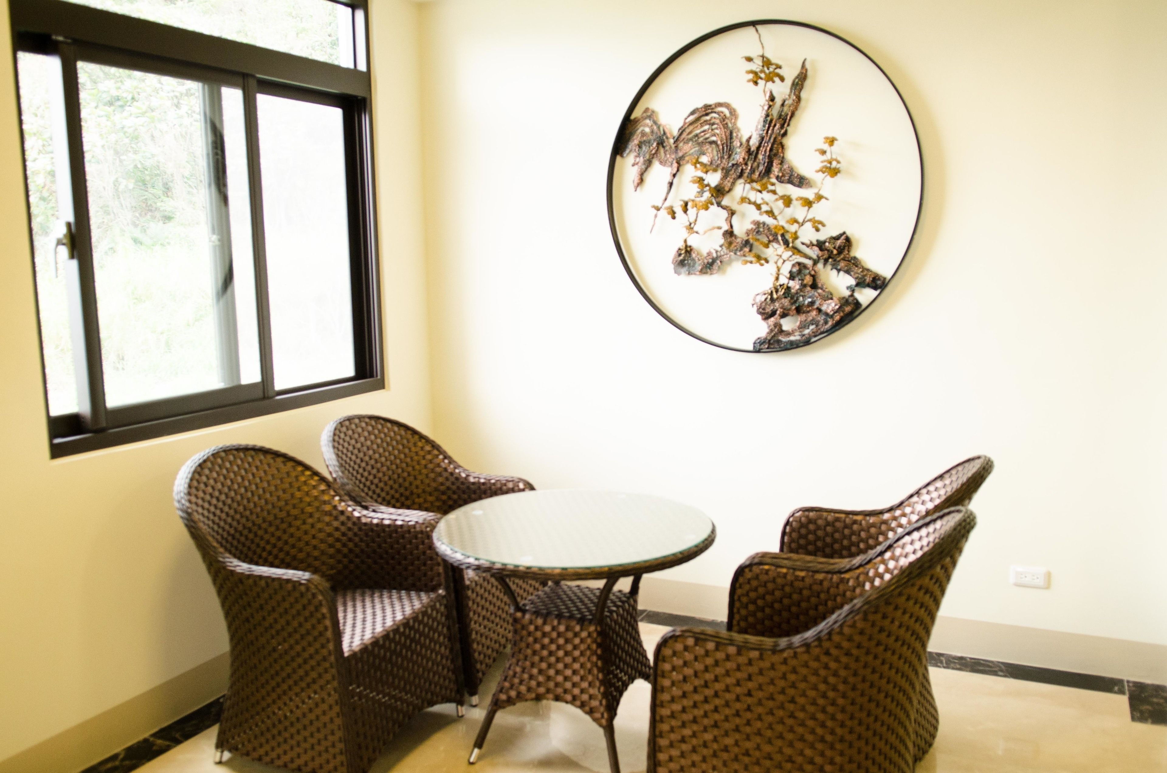 A dining area with wicker chairs and a round table, a window with blinds, and a wall-mounted artwork.