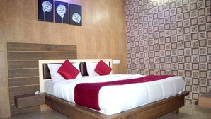 A modern bedroom with a wooden bed frame, white bedding, and red pillows. There are three framed artworks above the bed and a patterned wallpaper on the wall. - Sky Stays Heaven (Dwarka)