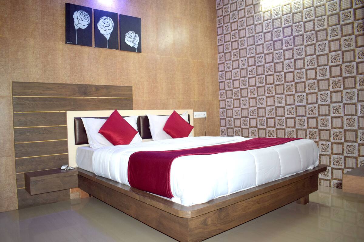 Une chambre moderne avec un cadre de lit en bois, une literie blanche et des coussins rouges. Trois œuvres d'art encadrées sont accrochées au-dessus du lit, et le mur est recouvert d'un papier peint à motifs.