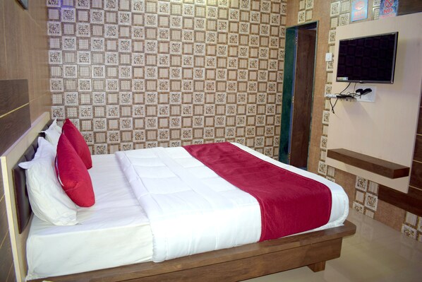 A neatly made bed with white and red bedding, a television mounted on the wall, and a patterned tile wall. - Sky Stays Heaven (Dwarka)