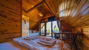Un dormitorio acogedor tipo cabaña de madera con una cama grande, una mesa de comedor y vistas por la ventana.