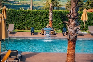 Una piscina con sillas de descanso y sombrillas, rodeada de vegetación y vistas al paisaje.