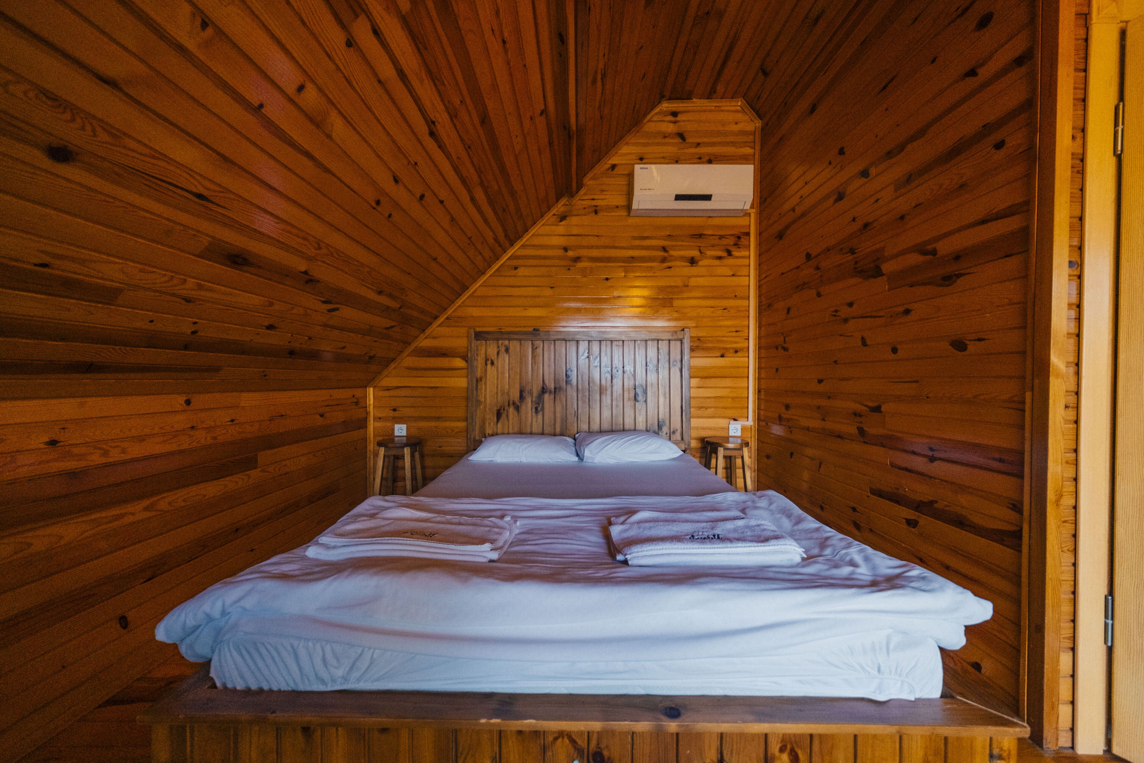 Quarto com painéis de madeira, uma cama e cabeceira de madeira, e um ar-condicionado fixado na parede.