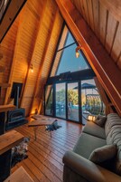 Un interior acogedor con techo inclinado, piso de madera, un sofá, una mesa y vistas al exterior.