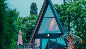 Un edificio moderno de forma triangular con terraza de madera y ventanas de vidrio, rodeado de exuberante vegetación.