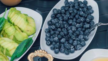 Une table dressée pour le petit-déjeuner avec des tranches d’avocat, des myrtilles, un bol de fraises, un pichet contenant un liquide brun et une assiette avec deux œufs au plat.