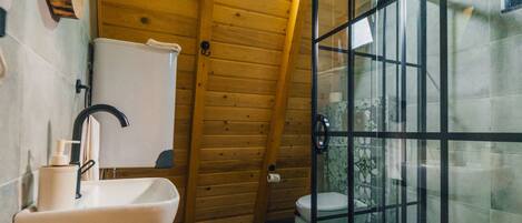 A wooden-paneled bathroom with a sink, toilet, and shower enclosure.