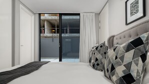 A modern hotel room with a large bed, a sliding glass door leading to a balcony, and a framed picture on the wall.