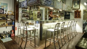 Zona de bar con mostrador, taburetes y estantes llenos de botellas.