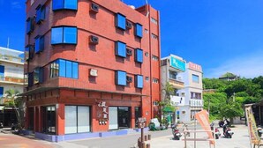 Un edificio rojo de varios pisos con una planta baja comercial, que cuenta con un amplio escaparate de vidrio y un letrero con caracteres chinos.
