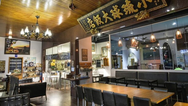 Interior de restaurante con techo de madera, lámparas colgantes y un gran letrero negro con letras doradas.