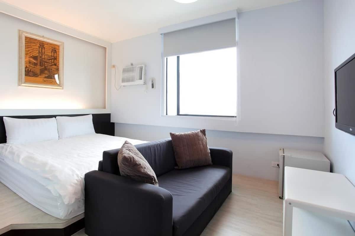 A modern hotel room with a bed, a sofa, a TV, and a window.