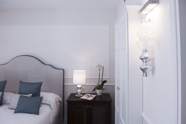 Un dormitorio con una cama, una mesita de noche con lámpara, una planta en maceta y un aplique de pared.